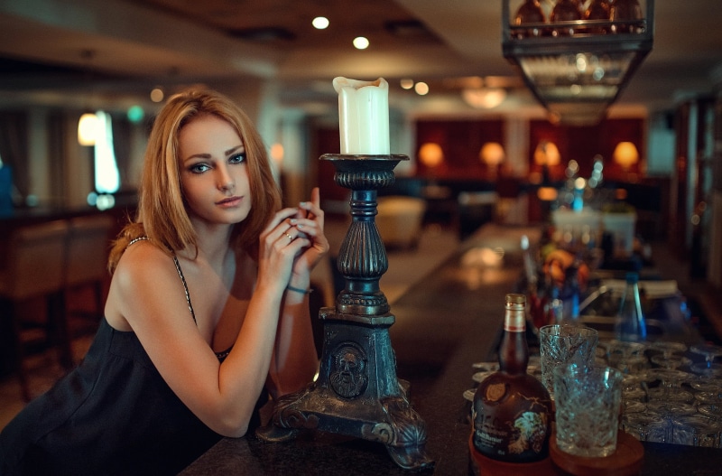food and drink, glass, alcohol, portrait, bottles, adult, bar - drink establishment, lifestyles, sitting, beautiful woman, candles, bar counter, young adult