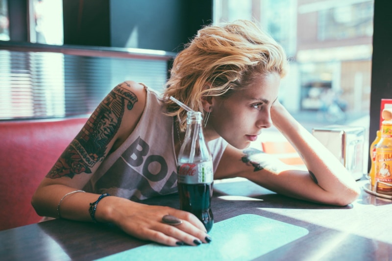 leisure activity, tattoo, hair, sitting, indoors, casual clothing, glass, young adult, lifestyles, drink, looking away, day, contemplation, blond hair