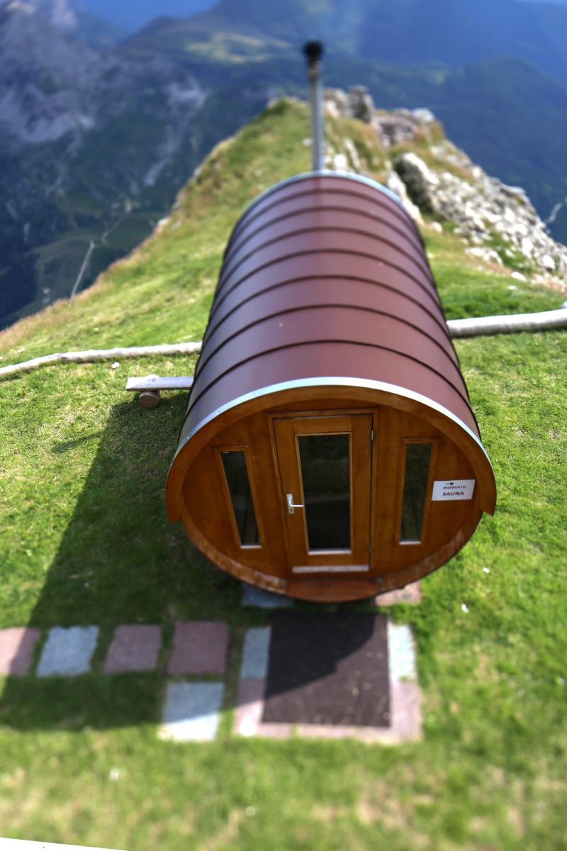 mountain, field, shadow, green color, cabin, sunlight, land, wood - material, mountain sauna, close-up, building exterior, outdoors, focus on foreground