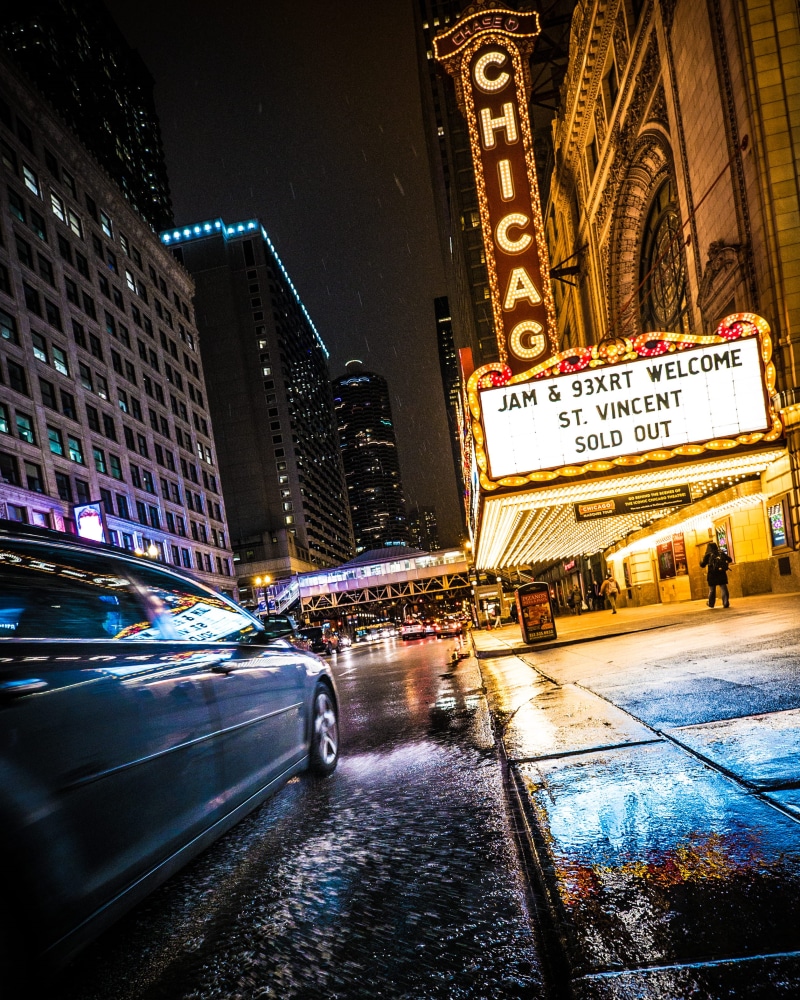 chicago theatre, illuminated, motor vehicle, architecture, road, city street, city life, land vehicle, rain, nighttime, people, signage, building exterior