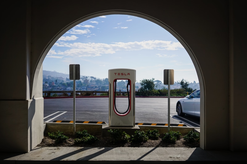 arch, vehicle, transportation, street, supercharger, day, near, tree, charger, architecture, city, mode of transportation, cloud - sky, bushes, text, sky