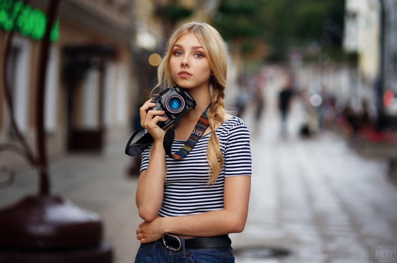 looking at viewer, 720P, photography themes, technology, blonde, long hair, filming, hair, Zenit (camera), beautiful woman, city, looking at camera, young adult