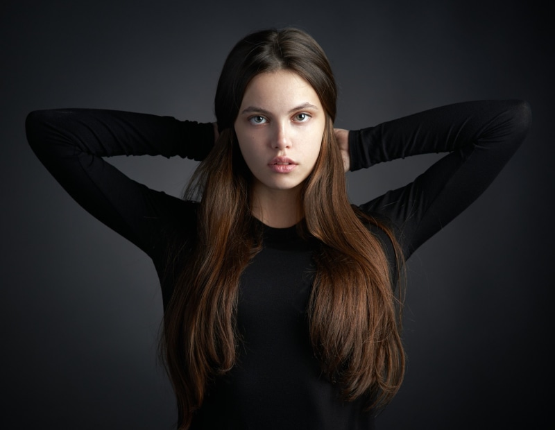 hands on head, young adult, 2K, standing, teenager, face, young women, beauty, hair, looking at camera, indoors, hairstyle, front view, long hair, black clothing