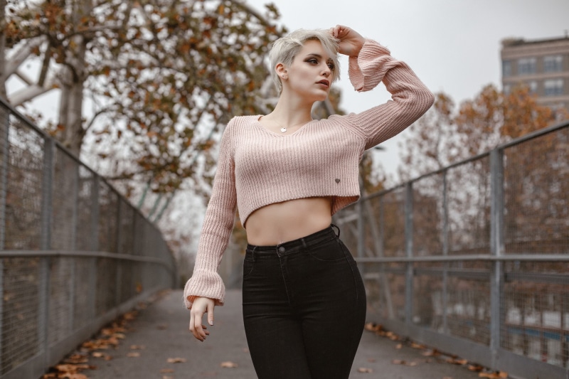 pierced navel, bokeh, short hair, hands in hair, jeans, necklace, 1080P, standing, looking away, high waisted, white hair, portrait, women outdoors, blonde