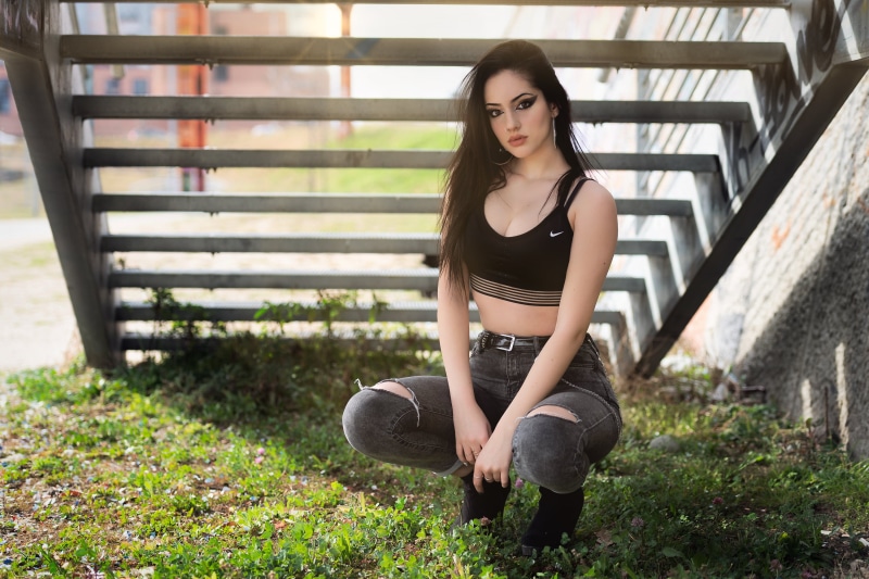 stairs, cleavage, outdoors, looking at viewer, nose rings, belly, jeans, eyeliner, pink lipstick, model, brunette, torn jeans, depth of field, chains, short tops
