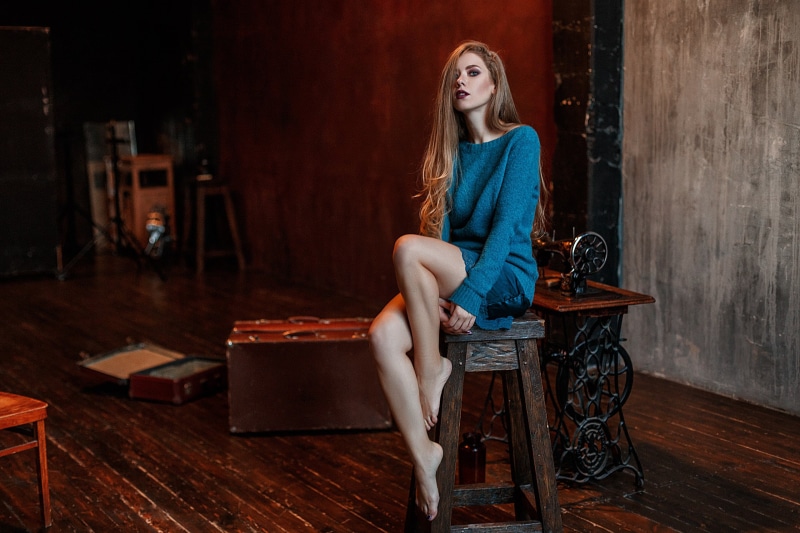 beautiful woman, looking at viewer, seat, adult, portrait, long hair, chair, wooden floor, blue sweater, sitting, clothing, waiting, women, beauty, indoors