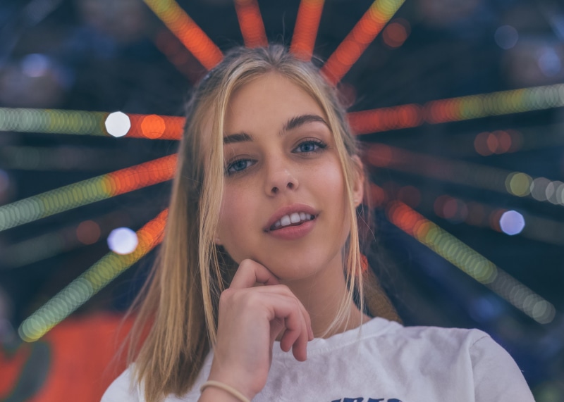 model, depth of field, face, women, smiling, blonde, touching face, 1080P, women outdoors, outdoors, open mouth, white t-shirt, looking at viewer, portrait