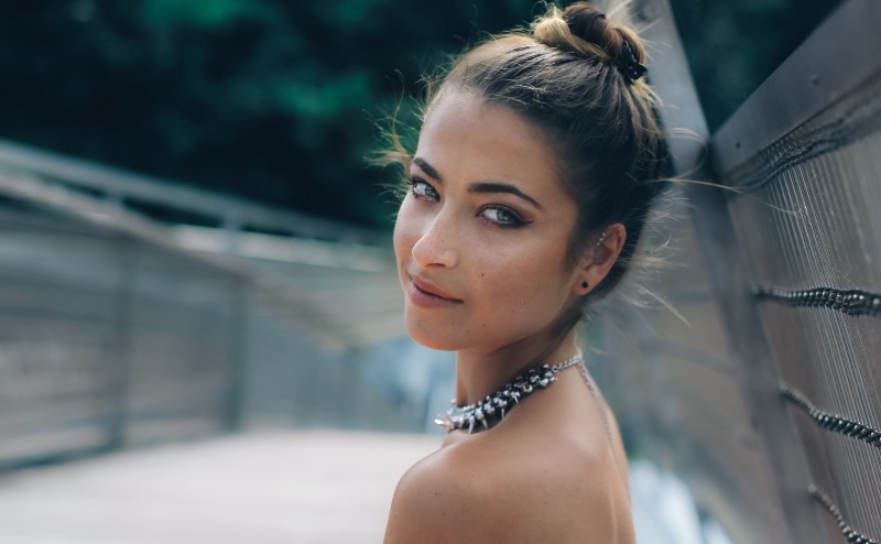 necklace, hairstyle, brunette, headshot, outdoors, fashion, beautiful woman, buns, lifestyles, depth of field, looking at camera, bridge, contemplation
