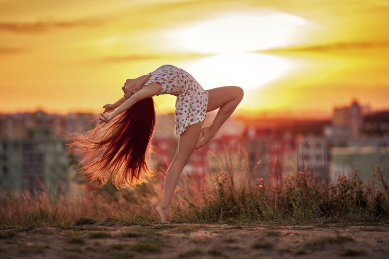 hairstyle, depth of field, arched back, young adult, outdoors, adult, sky, land, leisure activity, long hair, sunset, nature, motion, city, one person