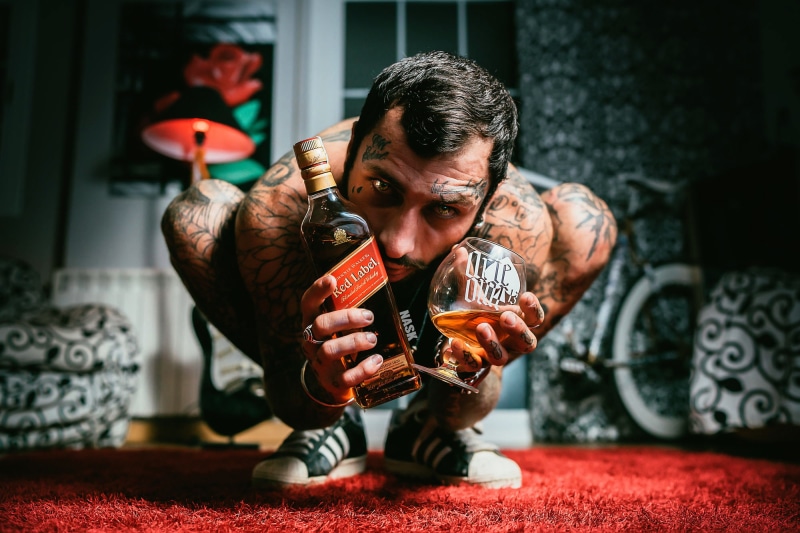 facial hair, men, one person, red, bottles, young men, front view, young adult, sitting, real people, leisure activity, 1080P, whisky, tattoo, lamp, mature adult