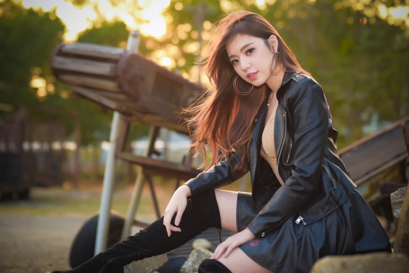 necklace, Asian, women outdoors, 2K, hoop earrings, knee-high boots, black clothing, long hair, brown eyes, sitting, skirt, Kiki Hsieh, smiling, leather jackets