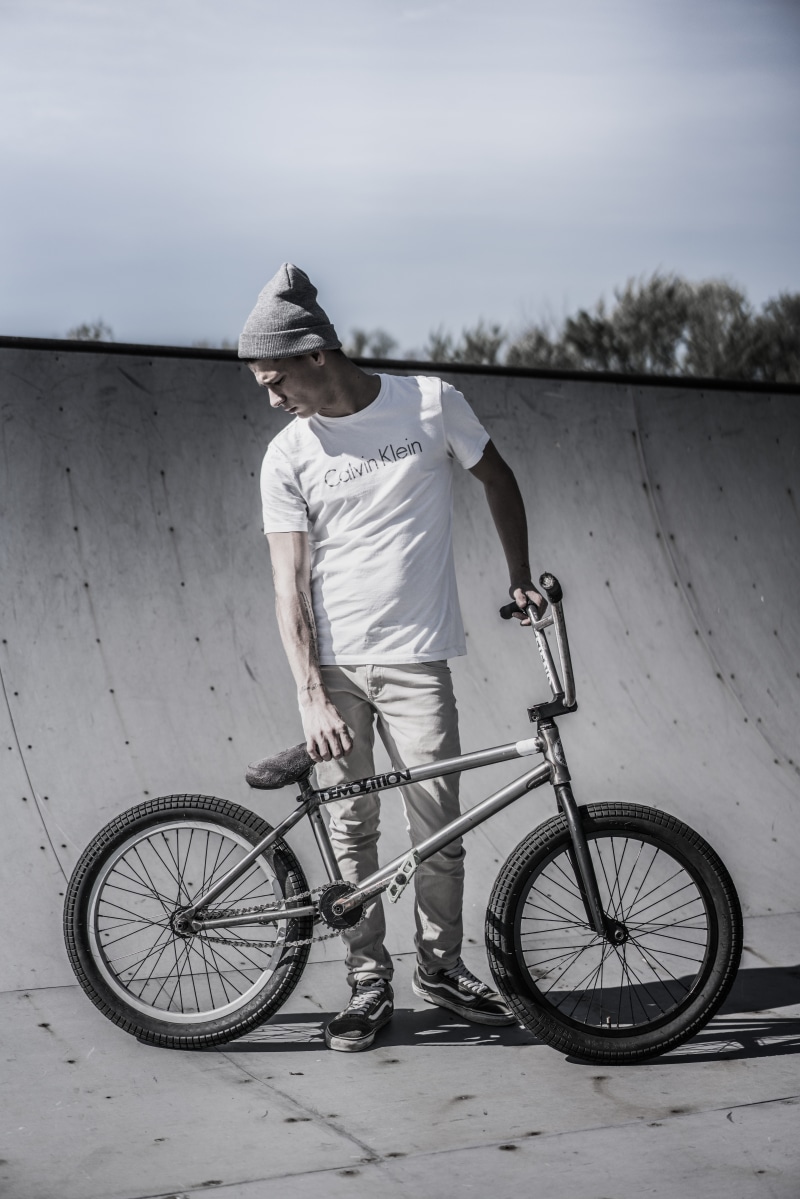 photo, grayscale, holding, track, casual clothing, bicycle, near, hat, lifestyles, one person, males, bmx, standing, 8K, men, calvin klein, helmet, outdoors