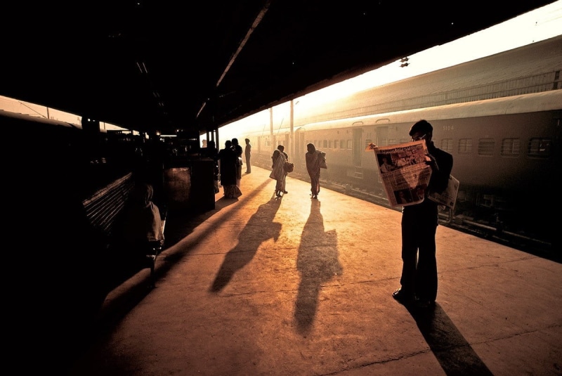 travel, sun rays, newspapers, real people, India, men, train station, vintage, lifestyles, reading, outdoors, sitting, 480P, transportation, sunset, railroad station platform