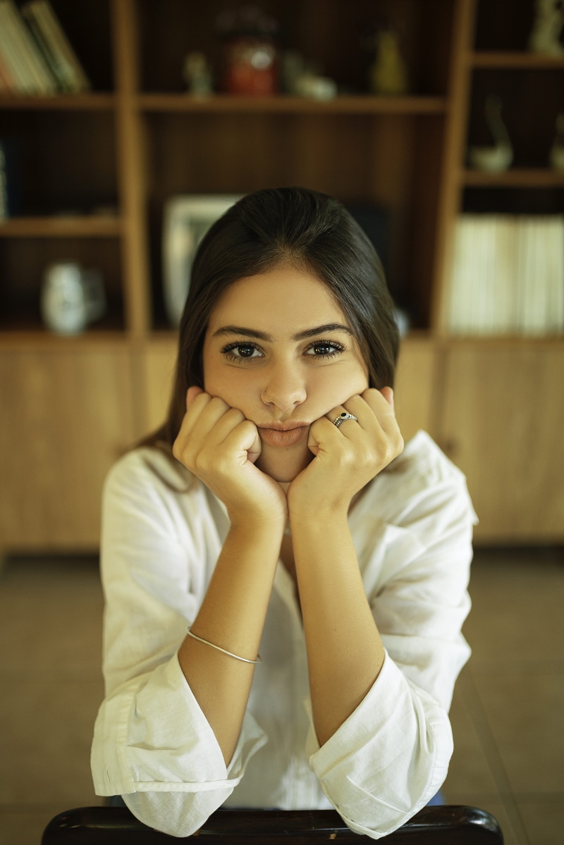 beautiful woman, indoors, hand, young adult, one person, lifestyles, sitting, real people, 5K, cute, adult, looking at camera, front view, looking, focus on foreground