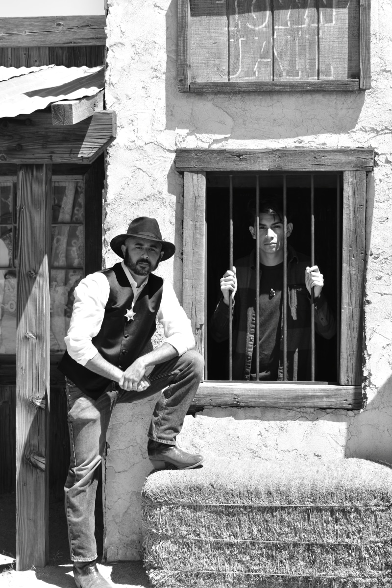 hat, young men, western, man, jail house, males, cowboy, wearing, west, sheriff, outdoors, building, black and white, full length, real people, wild, fedora