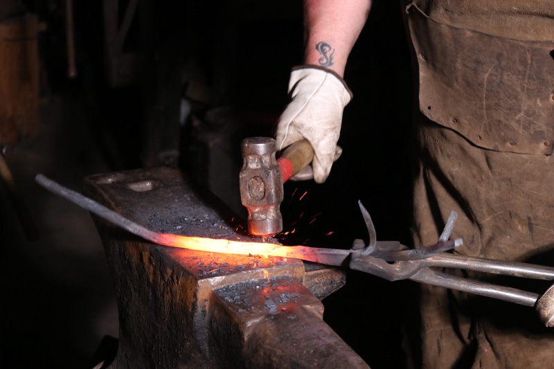 one person, indoors, preparation, heat - temperature, working, hand, human hand, hammer, melting, skill, occupation, forge, industry, blacksmith, burning