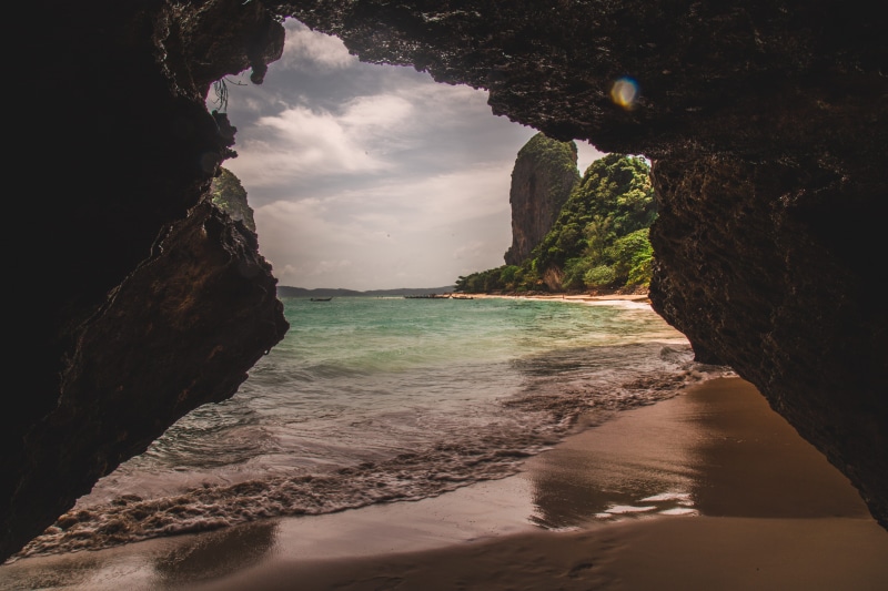 cave interior, near, land, railay beach, stack rock, dirt road, sky, boat, tranquility, forest, rock formation, explore, sand, beach, scenics - nature