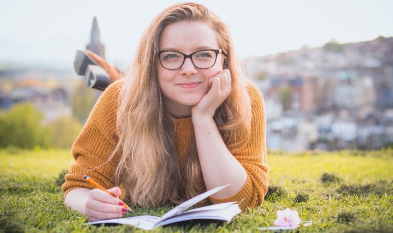 architecture, eyeglasses, enjoyment, grass, one person, leisure, pencil, outdoors, sit, smile, young adult, college, glasses, fashion, casual, care, headshot