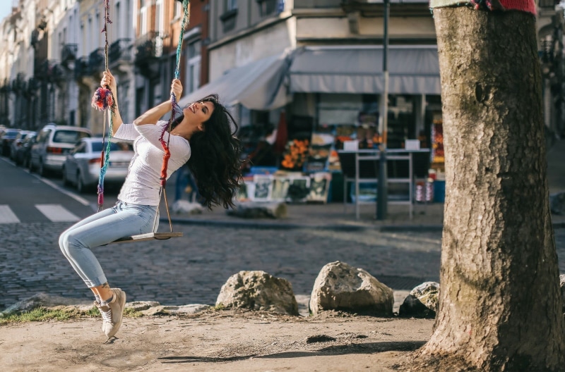 lifestyles, city, trees, building exterior, women, closed eyes, hair, young women, jeans, swings, brunette, leisure activity, day, smiling, long hair, full length