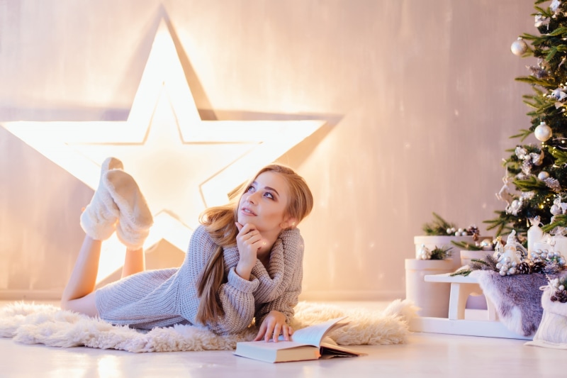 model, slippers, 2K, lying on front, sweater, women, on the floor, presents, blonde, feet in the air, looking up, sweater dress, long hair, books, smiling