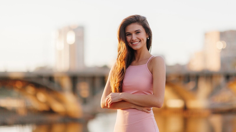 arms crossed, brunette, women, pink dress, bokeh, brown eyes, Pavel Vozmischev, pearl earrings, 720P, smiling, looking at viewer