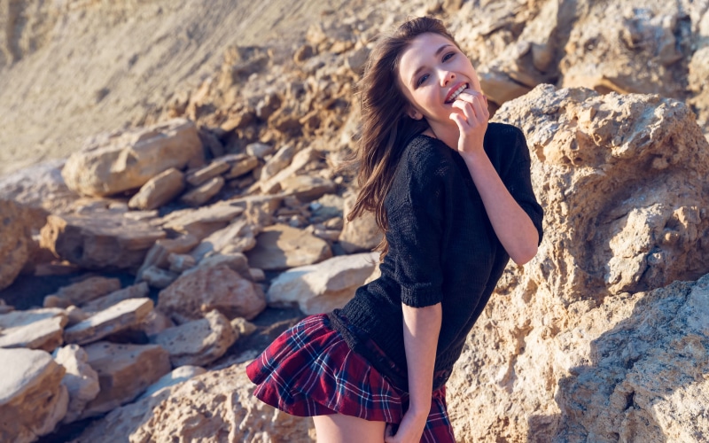skirt, 4K, looking at viewer, Mila Azul, rocks, black sweater, smiling