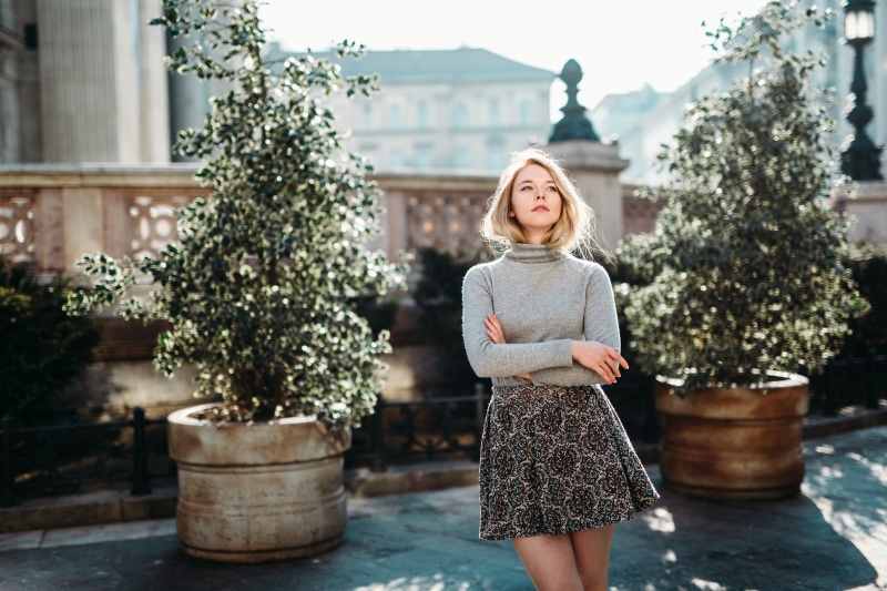 depth of field, hairstyle, sweater, day, gray, front view, real people, plant, blond hair, women outdoors, turtlenecks, skirt, standing, focus on foreground