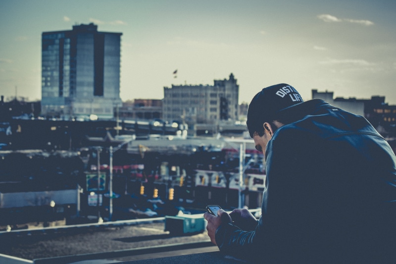 built structure, guy, nature, side view, focus on foreground, hat, people, adult, outdoors, iphone, clothing, hood, looking, architecture, adults only