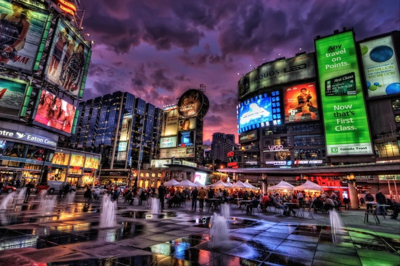 architecture, lifestyles, city street, buildings, advertisement, building exterior, gray, real people, illuminated, text, rain, cityscape, concrete, city life