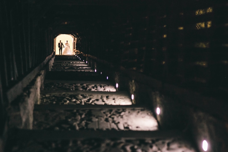lighting equipment, people, built structure, stairs, rail, dress, 2K, indoors, building, cellar, photo, old, dark, woman, lights, tunnel, man, low angle view