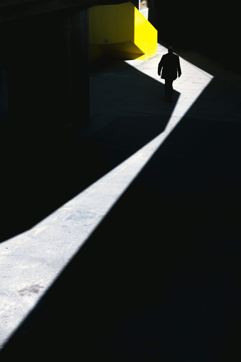 person, shadow, architecture, urban, lifestyles, path, lonely, man, built structure, alone, real people, high angle view, full length, standing, concrete