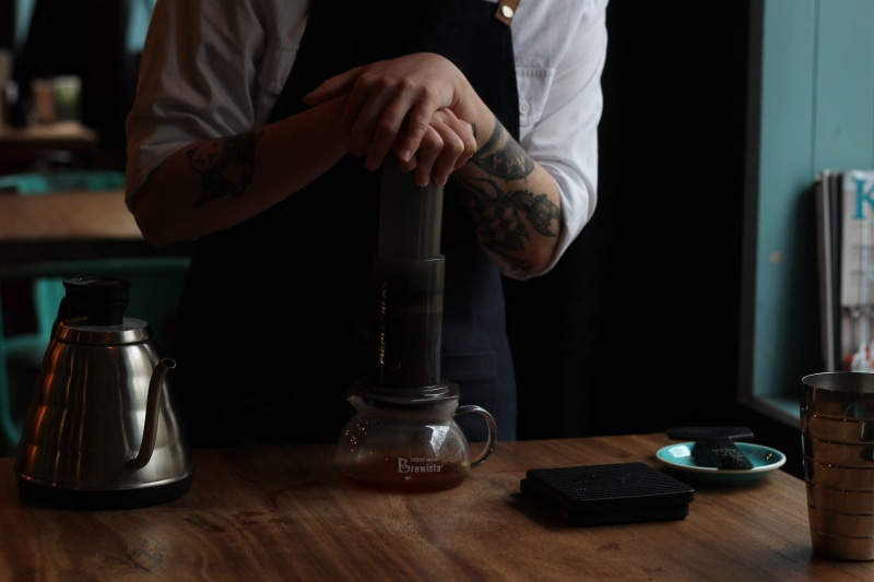 human body part, bottle, teapot, real people, person, home interior, one person, barista, table, coffee, hands, coffee cup, coffee shop, wooden table, human hand