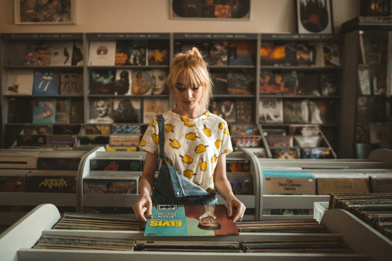 inside, woman, females, record, hairstyle, emotion, music, standing, blond hair, store, rack, record shop, front view, coffee shop, vinyl, happiness, indoors