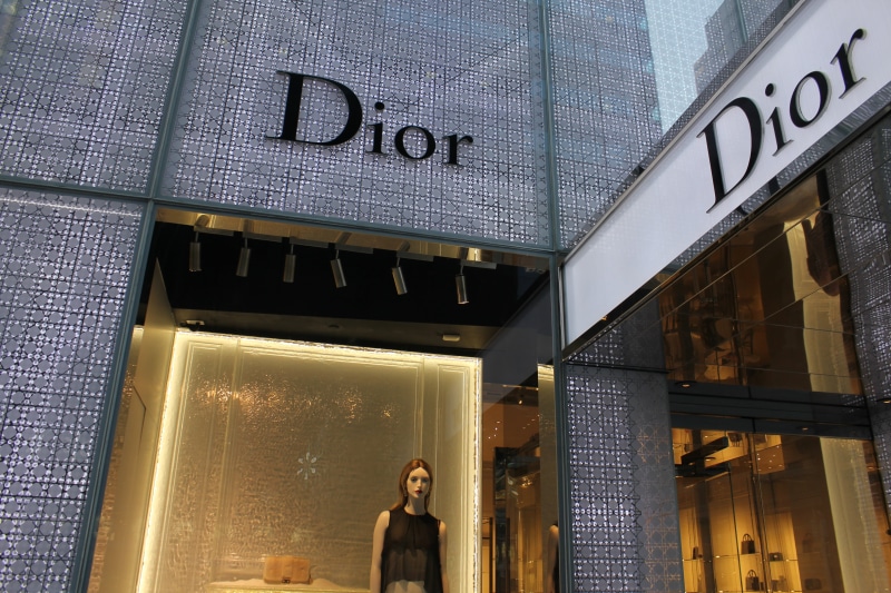 western script, built structure, front, standing, illuminated, communication, day, outdoors, one person, building exterior, low angle view, sign, dior