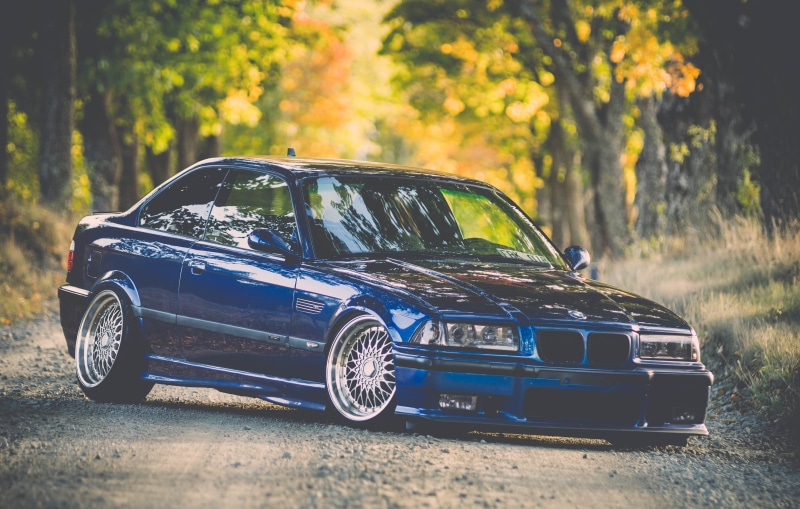 grille, sunlight, looking At View, mode of Transport, wheel, sports Car, outdoors, blue, focus on foreground, stance, design, car, nature, no People, land