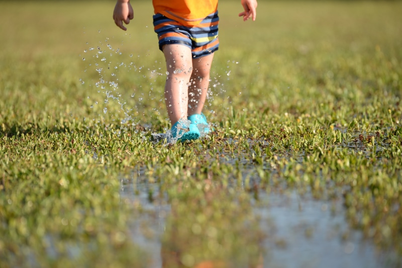 real people, water drops, outdoors, motion, feet, leisure activity, lifestyles, green color, grass, surface level, one person, shorts, mud, sunlight, sport