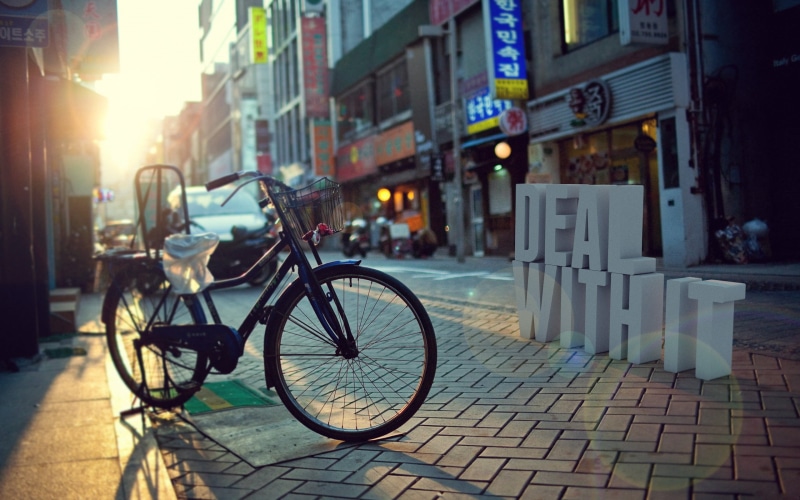 depth of field, stationary, city life, city, daytime, building, outdoors, lens flare, road, black, incidental people, street, bike, 2K, land vehicle, near