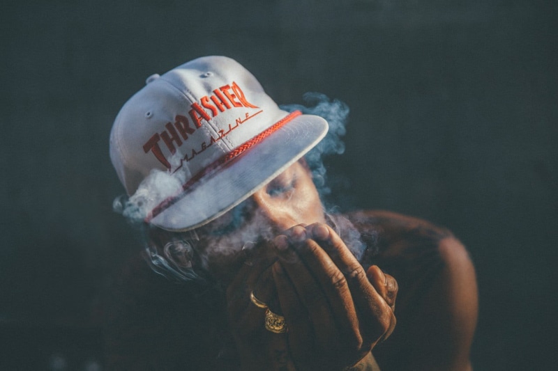 western script, Boo Johnson, photography, communication, street wear, hat, waist up, sign, smoke - physical structure, white, rings, Thrasher, van styles