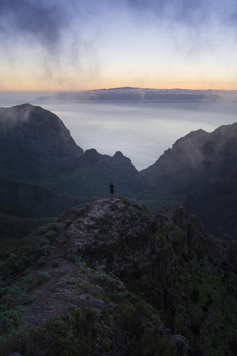 hiking, sky, water, leisure activity, landscape, rock, outdoors, one person, cloudy, sunrise - Dawn, hill, environment, cloud - Sky, aerial view, silhouette