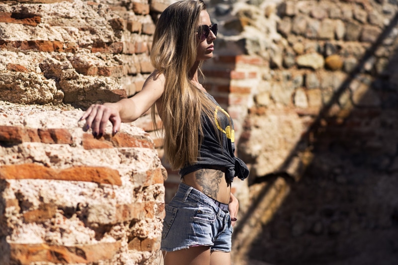 outdoors, day, skinny, young women, wall, standing, brick wall, belly, bricks, blonde, hairstyle, stone wall, wall - building feature, hair, depth of field
