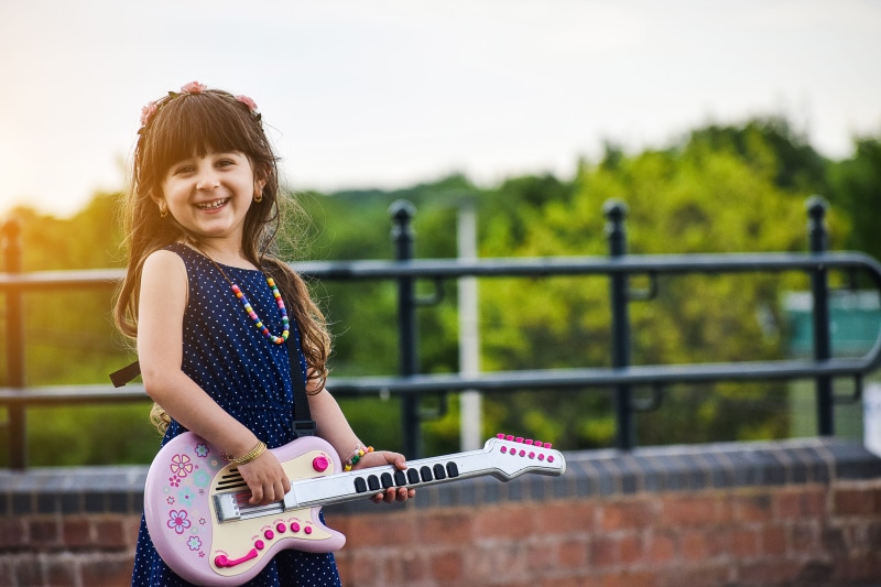 looking at camera, sound, day, pupil, human, pretty, smiling, guitar, hair, casual clothing, little, railing, playful, 5K, spring, hairstyle, musical