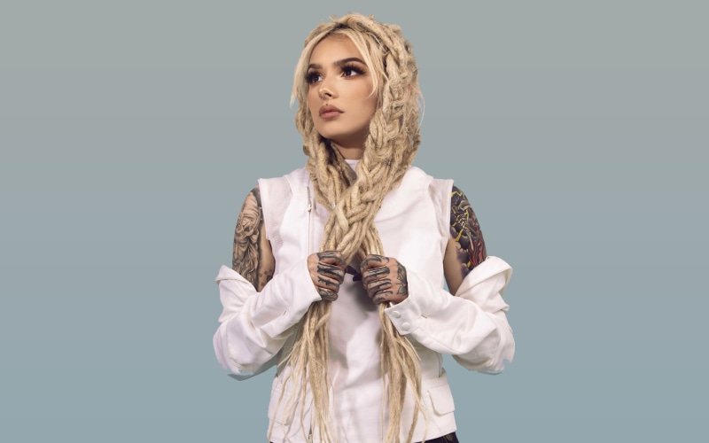 tattoo, makeup, model, ink, pierced nose, blonde, eyelashes, braids, 4K, white clothing, dyed hair, holding hair, dreadlocks, dark eyes, simple background
