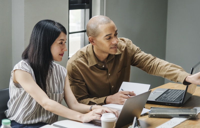 looking, cup, woman, two people, coworker, people, listening, colleagues, real people, desk, pointing, together, room, coffee, using laptop, indoors, discussing
