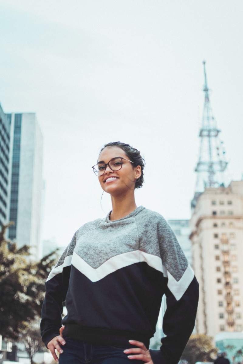 sweater, smiling, close-up, focus, gray, person, standing, sunglasses, daytime, building, women, focus on foreground, contemporary, female, casual clothing
