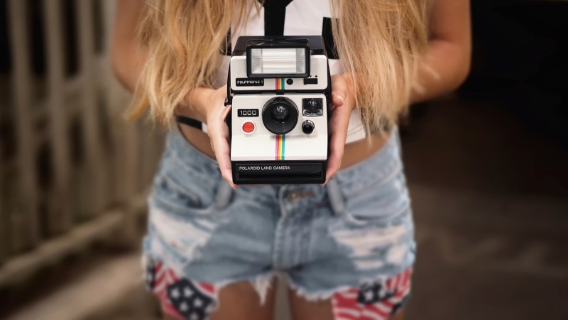 front view, obscured face, standing, filming, fujifilm, photography themes, one person, indoors, focus on foreground, camera - photographic equipment, activity