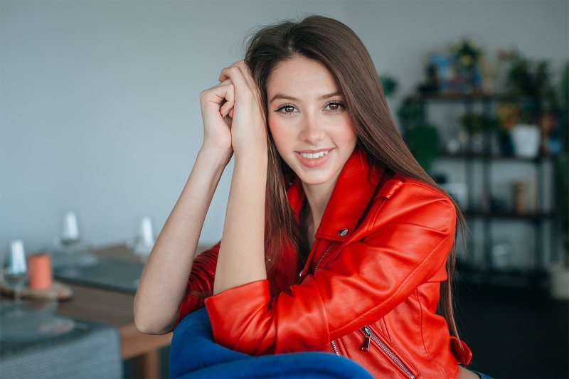 1080P, looking at viewer, leather jackets, brunette, model, smiling, face, jacket, red jackets, table, women indoors, depth of field, long hair, portrait