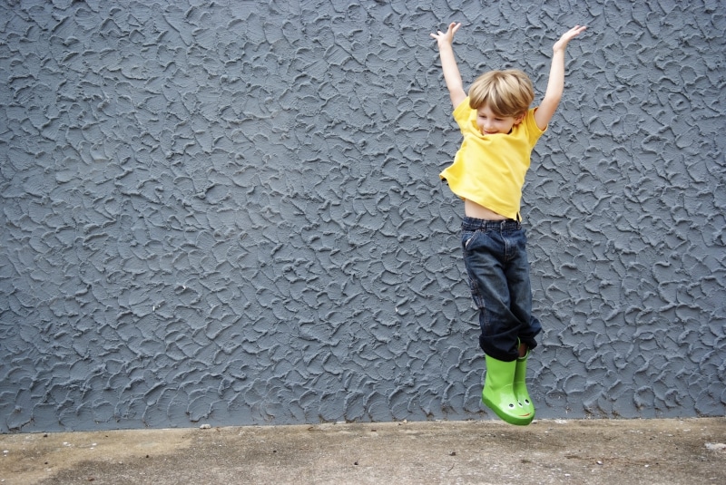 childhood, jump, grey, happy boy, copyspace, one person, full length, wall - building feature, blond hair, boy, day, lifestyles, child, kid, casual clothing