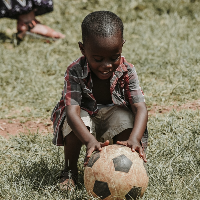 day, daytime, cool, men, football, soccer ball, child, nature, people, shorts, happy, boys, kid, real people, holding, smile, field, grass, front view
