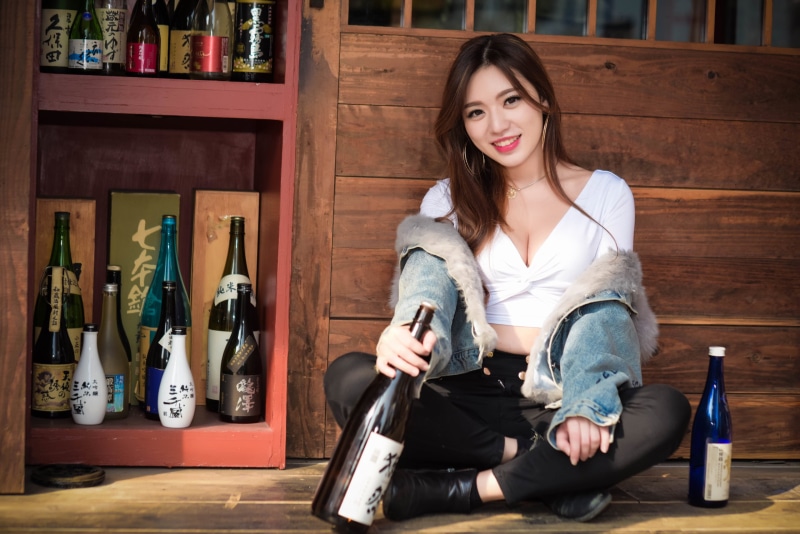 necklace, black pants, sitting, women, jacket, brown eyes, long hair, jeans jacket, looking at viewer, 2K, model, jeans, red lipstick, smiling, cleavage