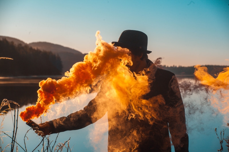 hat, warning sign, holding, male, smoke - physical structure, fire - natural phenomenon, flare, clothing, one person, men, flame, face, towards, sky, adult